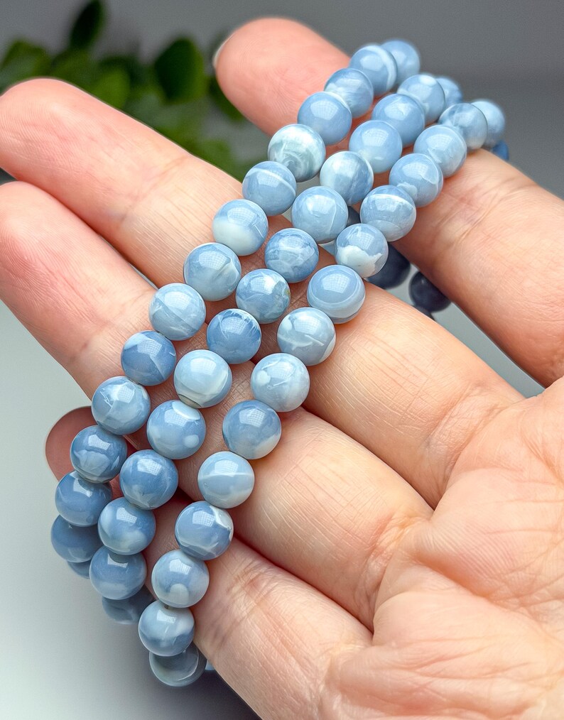 May include: A multi-strand bracelet composed of smooth, round, light blue beads with subtle white marbled patterns. The beads have a polished, glossy finish and are strung together in a continuous loop, showcasing a consistent spherical shape.