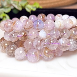 May include: A close-up of a multi-strand bracelet made of light pink and purple beads with gold and silver flecks. The beads are round and have a smooth, polished finish.