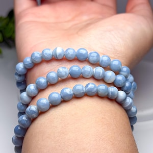 May include: A multi-strand bracelet composed of smooth, round, light blue beads with subtle white marbled patterns. The beads are strung together in a continuous loop, creating a layered appearance when wrapped around the wrist multiple times.