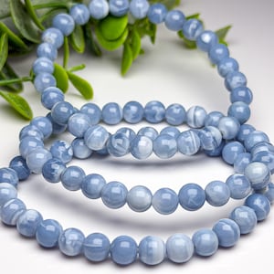 May include: A stretch bracelet composed of smooth, round, light blue beads with subtle white marbled patterns. The beads are uniform in size and arranged in a circular loop, showcasing a polished, reflective surface throughout the entire piece.