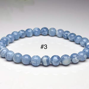 May include: A circular beaded bracelet featuring smooth, polished, light blue spherical beads with subtle white marbled patterns throughout. The bracelet is labeled with the text #3 in the center, showcasing a uniform arrangement of round stones.