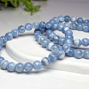 May include: A stretch bracelet composed of smooth, round, polished beads in shades of light blue and white. The beads feature a marbled, swirling pattern throughout their surface, creating a consistent appearance across the entire circular jewelry piece.