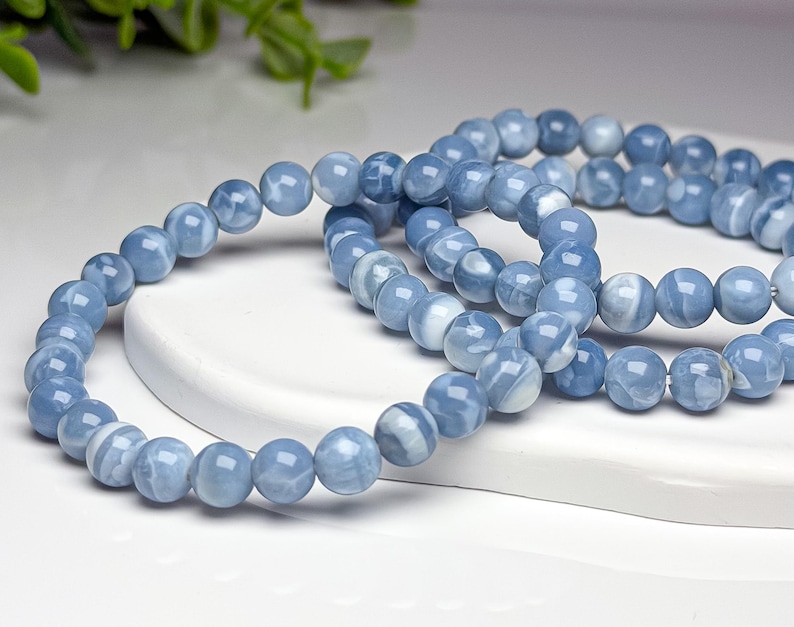 May include: A stretch bracelet composed of smooth, round, polished beads in shades of light blue and white. The beads feature a marbled, swirling pattern throughout their surface, creating a consistent appearance across the entire circular jewelry piece.
