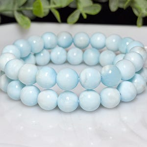 May include: A double-strand bracelet composed of smooth, round, light blue beads. The beads feature subtle white marbling and a polished finish, strung together on an elastic cord to form a circular shape with a consistent, uniform appearance.