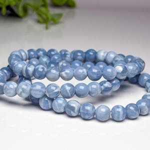 May include: A stretch bracelet composed of smooth, round, light blue beads with white marbled patterns. The beads are uniform in size and strung together on an elastic cord, creating a continuous circular loop of polished stone-like material.