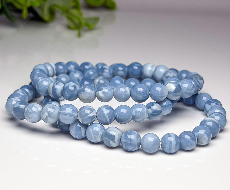 May include: A stretch bracelet composed of smooth, round, light blue beads with white marbled patterns. The beads are uniform in size and strung together on an elastic cord, creating a continuous circular loop of polished stone-like material.