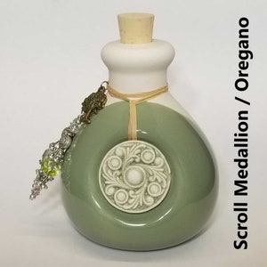 May include: A ceramic bottle with a white top and a green bottom. The bottle has a cork stopper and a decorative scroll medallion with the word "Oregano" on the side. The bottle has a charm with a tree design and green and silver beads.