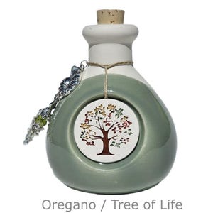 May include: A ceramic bottle with a cork stopper, painted in white and sage green. A round tag with a tree design hangs from the neck. A decorative silver spoon is attached to the bottle. The text "Oregano / Tree of Life" is at the bottom.