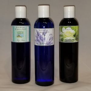 May include: Three glass bottles with blue, clear, and black liquid. Each bottle has a white cap and a label with the text "Reed Diffuser Fragrance Refill" and a different scent: "Fig Tree", "Lavender", and "Gardenia".
