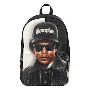 May include: Black and white backpack with a portrait of a man wearing sunglasses and a black baseball cap with the word "Compton" on it. The man has a black leather jacket and the text "N.W.A" is visible on the jacket.