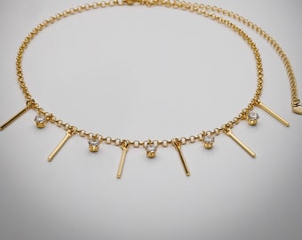 May include: A gold chain necklace with small, clear stones and dangling gold bars. The necklace is on a white background.