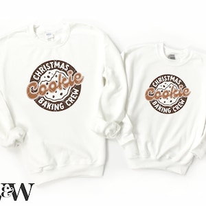 May include: Two white crewneck sweatshirts with a brown circle graphic that says "Christmas Cookie Baking Crew" with a brown cookie image in the center.