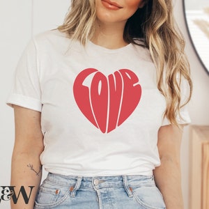 May include: White t-shirt with a red heart-shaped graphic that says "LOVE" in a retro font.