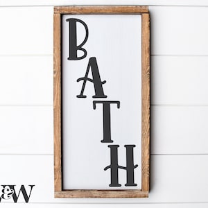 Könnte beinhalten: Ein Holzschild mit dem Wort "BATH" in schwarzen, stilisierten Buchstaben. Das Schild hat einen rustikalen braunen Rahmen.