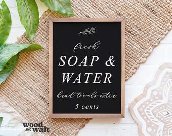 May include: A black chalkboard sign with white text that reads "fresh soap & water hand towels extra 5 cents". The sign is framed in wood and has a small leaf design in the top left corner.