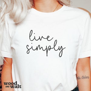 May include: White t-shirt with the text "live simply" written in black cursive script.