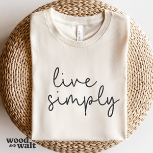 May include: A white t-shirt with the text "live simply" written in black cursive script.
