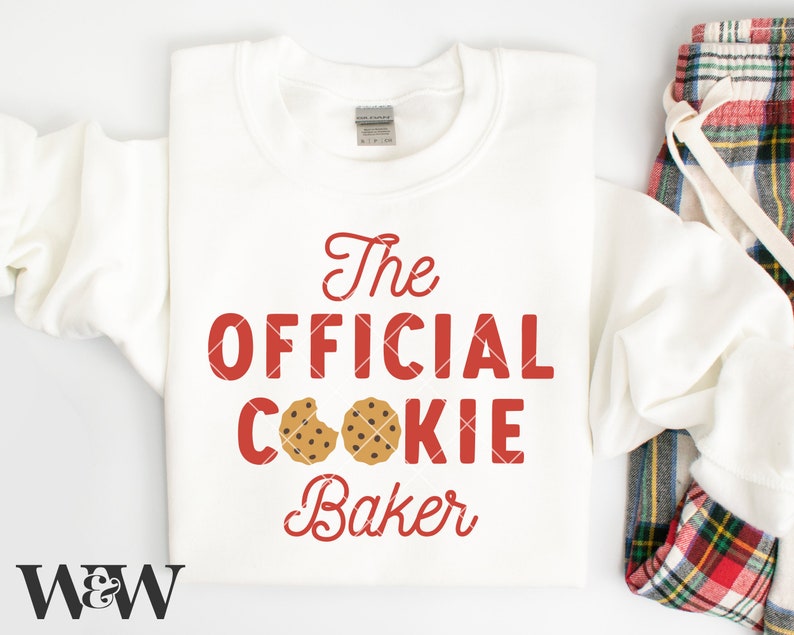 May include: White sweatshirt with red text that says "The Official Cookie Baker" with two chocolate chip cookies on the word "cookie".