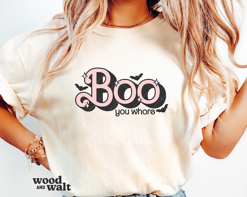 May include: Cream-colored t-shirt with the text "Boo you whore" in a retro font with pink and black accents. The design includes bats and stars, perfect for Halloween.