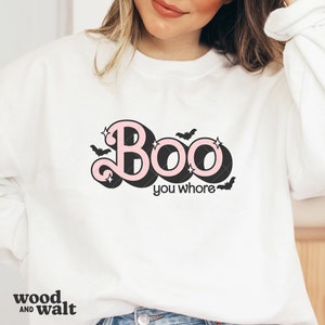 May include: White sweatshirt with the text "Boo you whore" in a pink and black design. The word "Boo" has a retro font with stars and bats. The sweatshirt is a crew neck style.