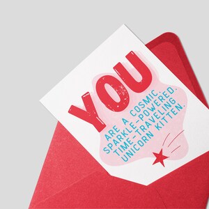 Puede incluir: Una tarjeta blanca con un dise&ntilde;o rosa y rojo. La tarjeta dice "YOU ARE A COSMIC. SPARKLE-POWERED. TIME-TRAVELING UNICORN KITTEN."