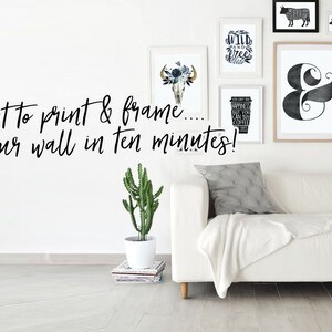 Op de afbeelding: Een witte bank met een witte deken en twee kussens. De muur achter de bank is versierd met zwart-witte ingelijste prints, waaronder een schedel met bloemen, een koffiekopje, een ampersand, een luipaard en een koe. De tekst "Art to print & frame... On your wall in ten minutes!" staat in zwart op de muur.