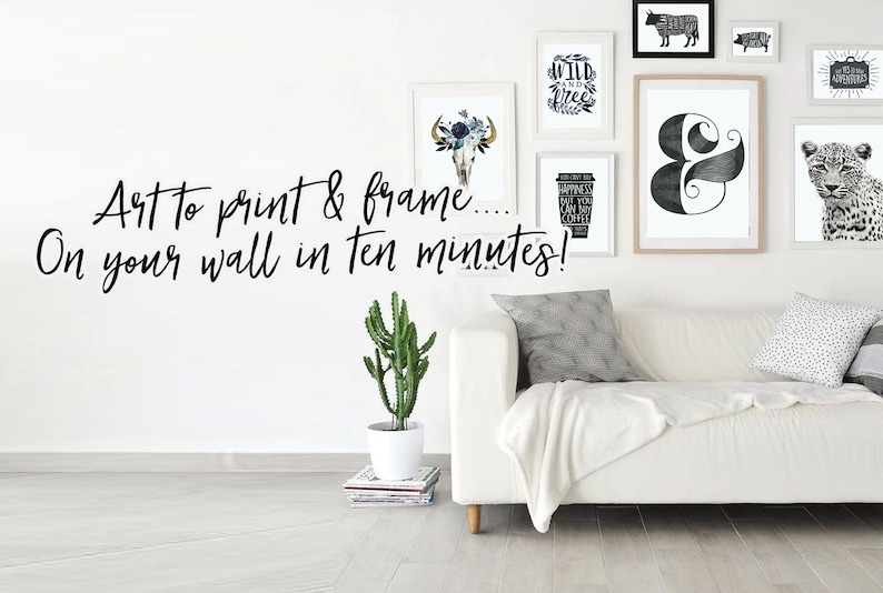 Op de afbeelding: Een witte bank met een witte deken en twee kussens. De muur achter de bank is versierd met zwart-witte ingelijste prints, waaronder een schedel met bloemen, een koffiekopje, een ampersand, een luipaard en een koe. De tekst "Art to print & frame... On your wall in ten minutes!" staat in zwart op de muur.