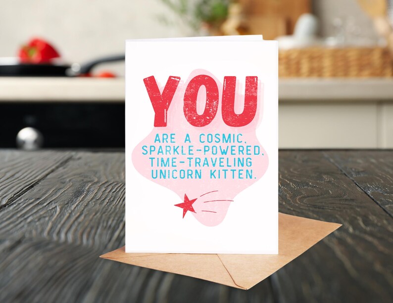 Puede incluir: Una tarjeta de felicitaci&oacute;n rosa y blanca con el texto "YOU ARE A COSMIC. SPARKLE-POWERED. TIME-TRAVELING UNICORN KITTEN." en letras azules y rojas.