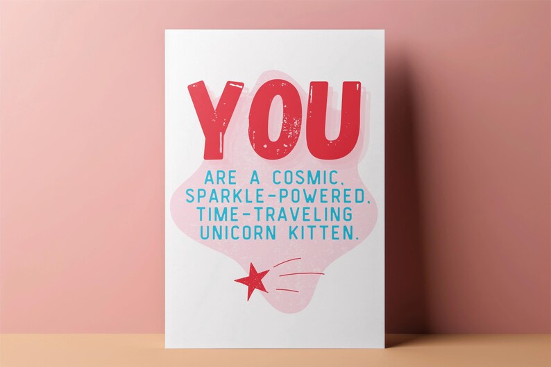 Puede incluir: Una tarjeta rosa y blanca con el texto "YOU ARE A COSMIC. SPARKLE-POWERED. TIME-TRAVELING UNICORN KITTEN." en letras azules y rojas. Una estrella roja con contorno blanco se encuentra en la esquina inferior derecha.