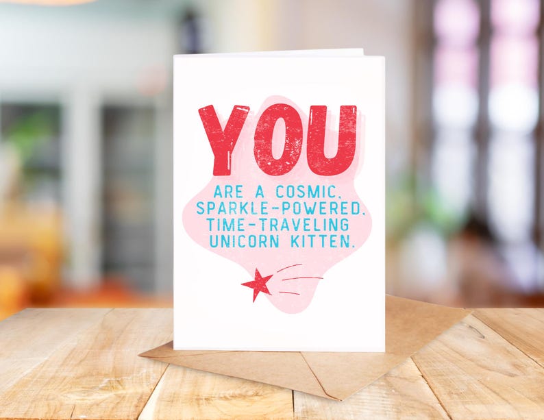 Puede incluir: Una tarjeta blanca con texto rosa y azul que dice "YOU ARE A COSMIC. SPARKLE-POWERED. TIME-TRAVELING UNICORN KITTEN." Hay una nube rosa con una estrella roja y una estrella fugaz azul.