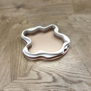 May include: A set of three nested trays in a unique organic shape. The trays are made of a light pink and white material and are perfect for displaying small items or serving snacks.