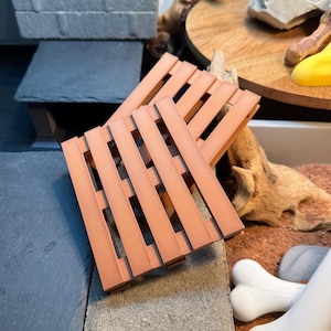 May include: Two brown wooden pallet-style coasters. The coasters are made of a light brown wood and have a rustic look.