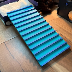 May include: A blue and teal ramp with horizontal ridges. The ramp is made of a solid material and is designed for small pets. The ramp is placed on a wooden surface.