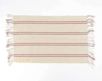 May include: A beige and pink striped woven rug with fringe on all sides. The rug has the text "HELPERN PETS" woven into the bottom edge.