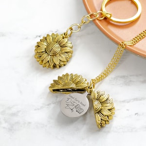 May include: A gold-colored sunflower pendant necklace and keychain. The sunflower pendant opens to reveal a silver charm with the text "Good Girls Read Dirty Books" and a book graphic. The keychain has a gold ring.