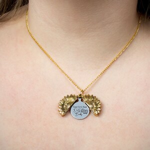 May include: A gold-colored necklace with a sunflower pendant. The pendant opens to reveal a circular charm with the text "Good Girls Read Dirty Books" and a book graphic. The necklace is worn around the neck.