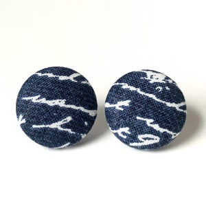 Pode incluir: Dois botões redondos revestidos de tecido azul marinho com um design abstrato branco. Os botões estão sobre um fundo branco. Estes botões podem ser usados para projetos de costura ou artesanato.