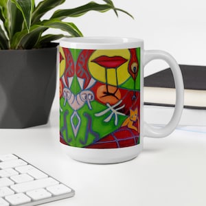 May include: White ceramic mug featuring a colourful abstract design. The design includes a red mouth, yellow and green shapes, and a small orange cat. The design is reminiscent of a surrealist painting.