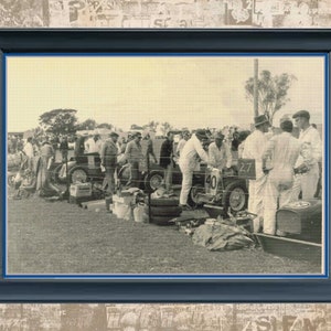 May include: A black and white vintage photograph of a group of people standing around a race car. The car is a classic open-wheeled race car with a number 40 on the side. The people are dressed in casual clothing and appear to be watching the race.