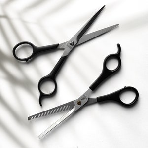 Może przedstawiać: Dwie pary czarnych nożyczek ze srebrnymi ostrzami. Jedna para ma ząbkowane ostrze, a druga proste. Obie pary mają nadrukowane numery na ostrzach.