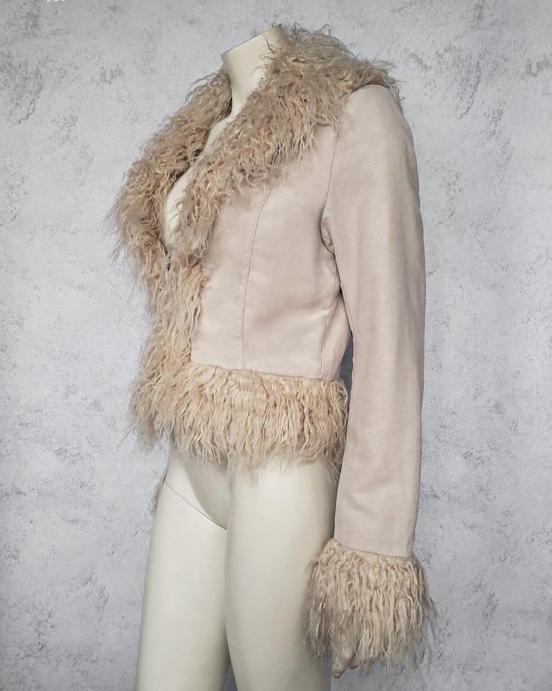 May include: A light beige jacket with a faux fur collar, cuffs, and hem. The jacket is made of a suede-like material and has a tailored fit. The faux fur trim adds a touch of luxury and texture to the garment.