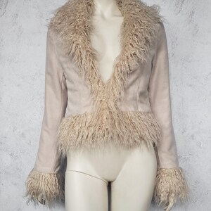 May include: A light beige jacket with a faux fur collar, trim, and cuffs. The jacket is displayed on a mannequin. The jacket has a suede-like texture and a tailored fit. The faux fur is a lighter shade of beige.