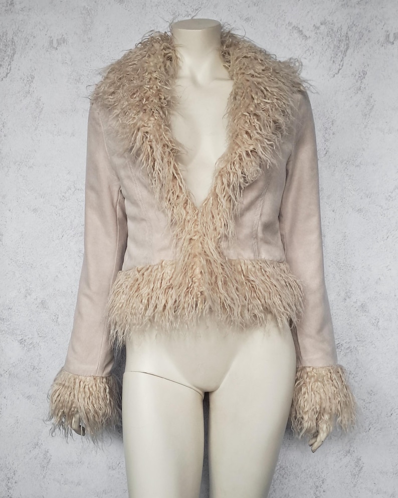 May include: A light beige jacket with a faux fur collar, trim, and cuffs. The jacket is displayed on a mannequin. The jacket has a suede-like texture and a tailored fit. The faux fur is a lighter shade of beige.