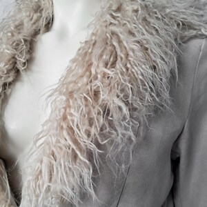 May include: A light gray faux suede jacket with a shaggy, light beige faux fur collar. The jacket has a classic lapel design and a soft, textured appearance. The faux fur collar adds a touch of luxury and warmth to the garment.