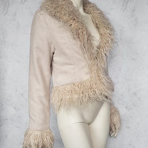 May include: A light beige jacket with a faux fur collar, trim, and cuffs. The jacket is displayed on a mannequin. The jacket has long sleeves and a cropped length. The faux fur is a lighter shade than the jacket.