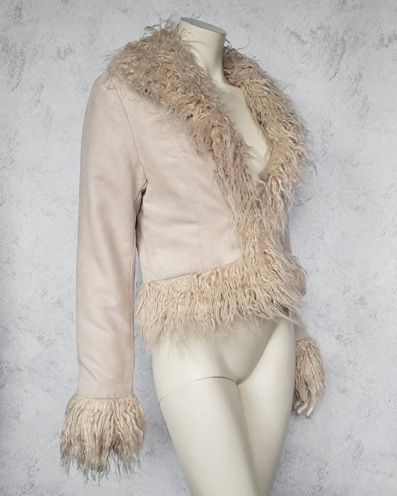 May include: A light beige jacket with a faux fur collar, trim, and cuffs. The jacket is displayed on a mannequin. The jacket has long sleeves and a cropped length. The faux fur is a lighter shade than the jacket.