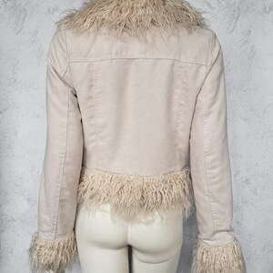 May include: A light beige jacket with a faux fur collar, cuffs, and hem. The jacket has long sleeves and a tailored fit. The faux fur is a light tan color, and the jacket appears to be made of a suede-like material. The jacket is displayed on a mannequin.