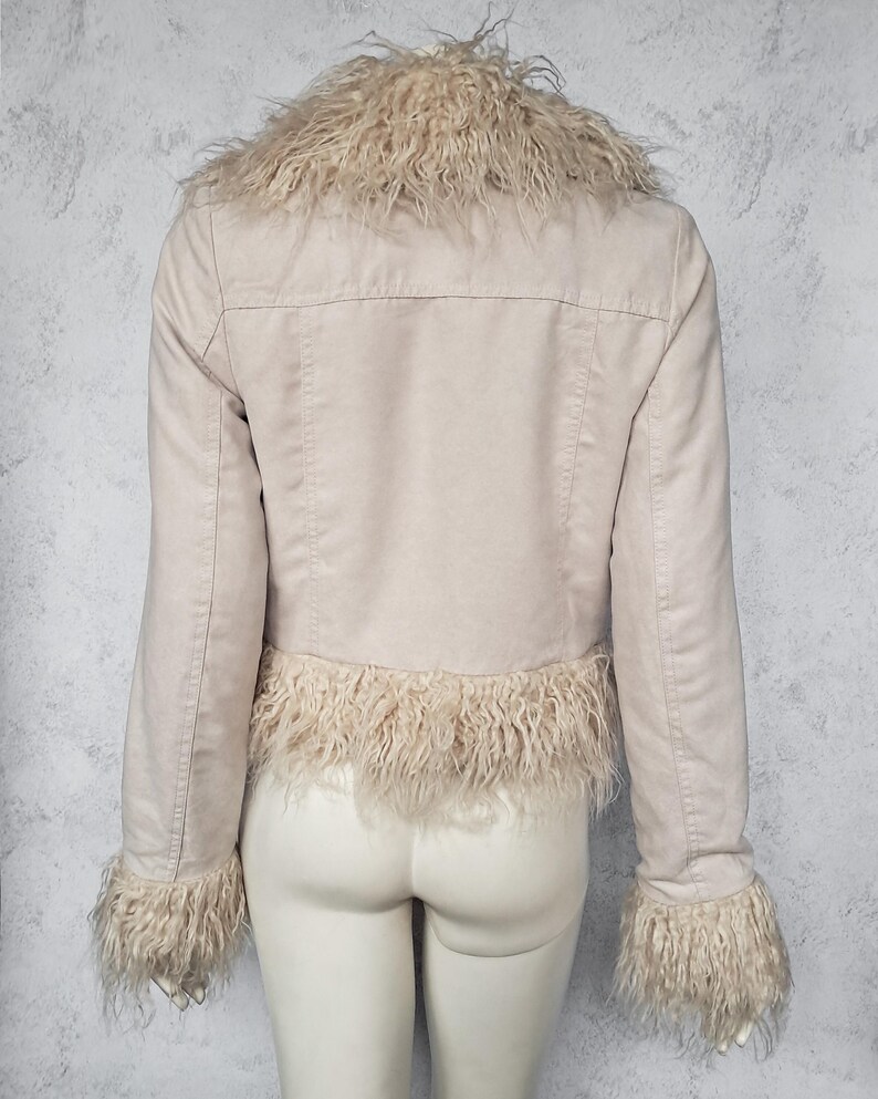May include: A light beige jacket with a faux fur collar, cuffs, and hem. The jacket has long sleeves and a tailored fit. The faux fur is a light tan color, and the jacket appears to be made of a suede-like material. The jacket is displayed on a mannequin.