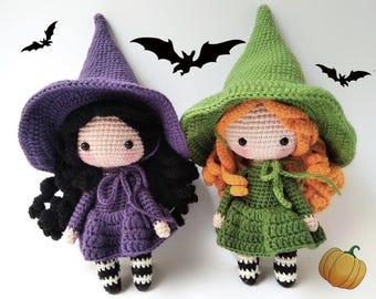 May include: Two crocheted witch dolls with black and orange hair, wearing purple and green dresses, black and white striped stockings, and pointed hats. A small orange pumpkin is in the background.