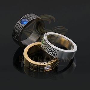 May include: Three rings with inscriptions and gemstones. One ring is silver with a blue gemstone and the year 1997. Another is gold with a clear gemstone and the year 2022. The third ring is silver with green text.